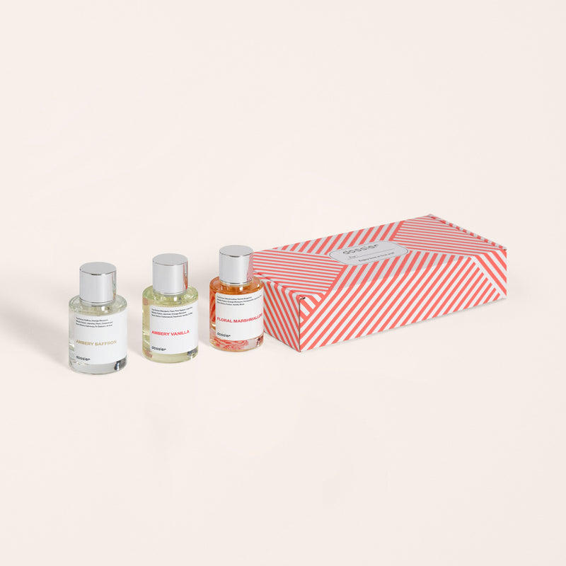 A set of three Dossier perfume bottles next to their red and white striped packaging box.